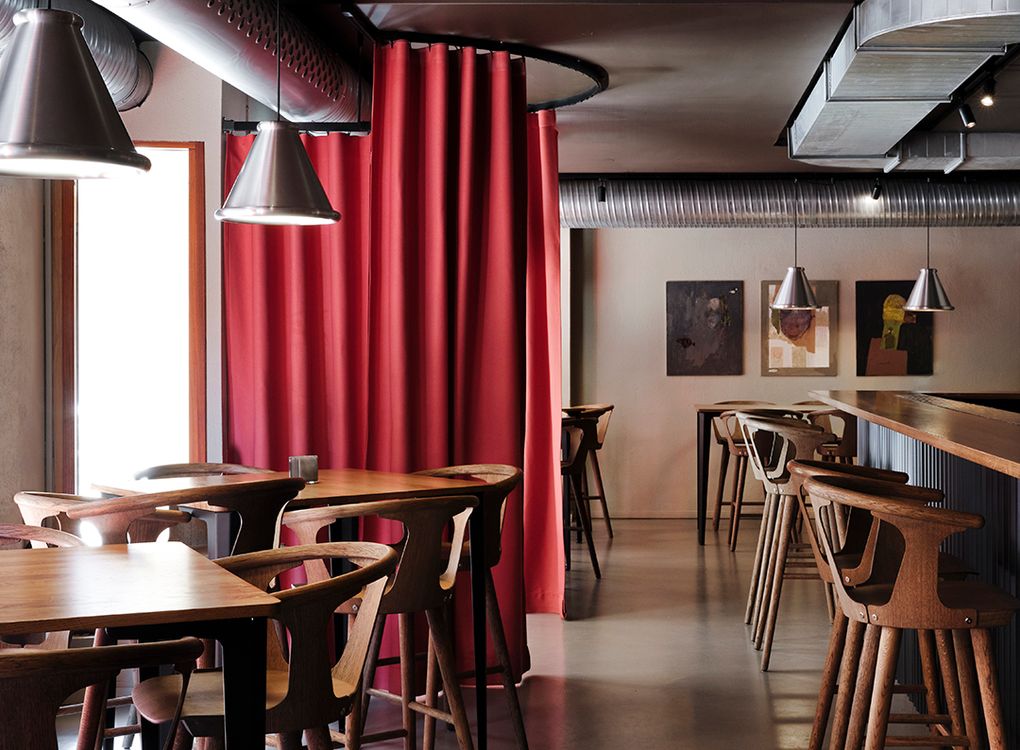 Belle-pendlar i metall från Belid Lighting Group lyser upp röda gardiner och höga trästolar på Blokk i Göteborg