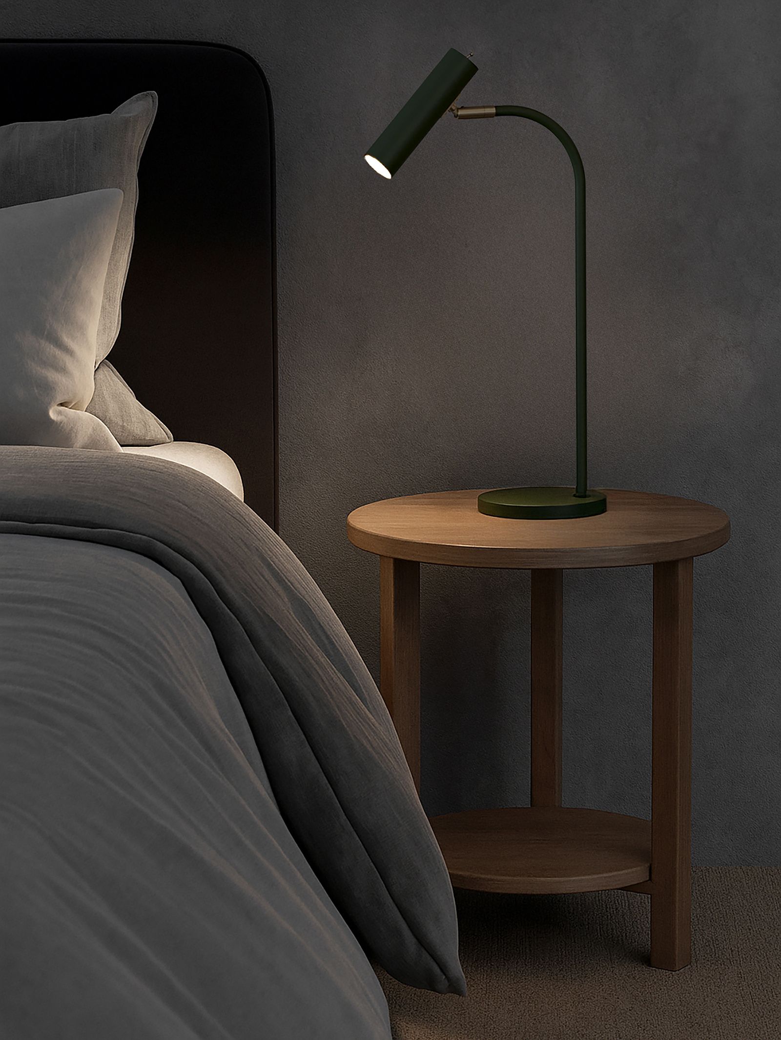 Slender table lamp in bottle green and brass beside a bed