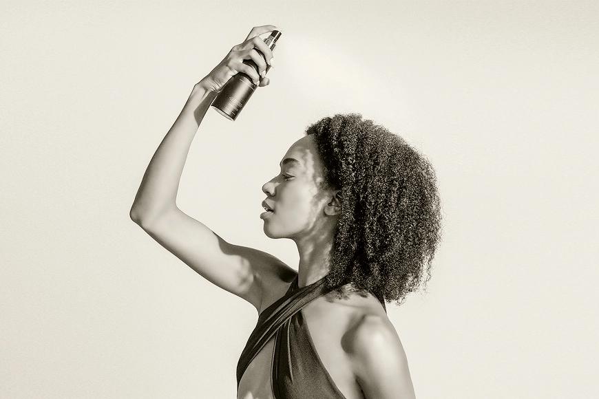 Woman with curly hair spraying a bottle of Uzima haircare product