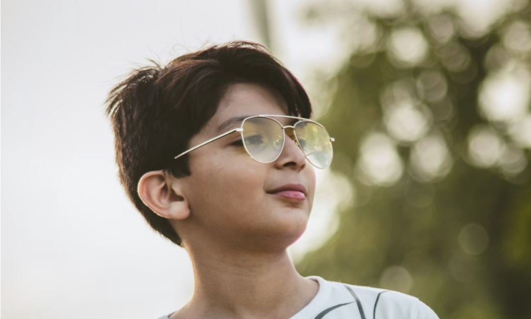 Glad dreng med nye børnebriller sidder ved skrivebord og læser i skole