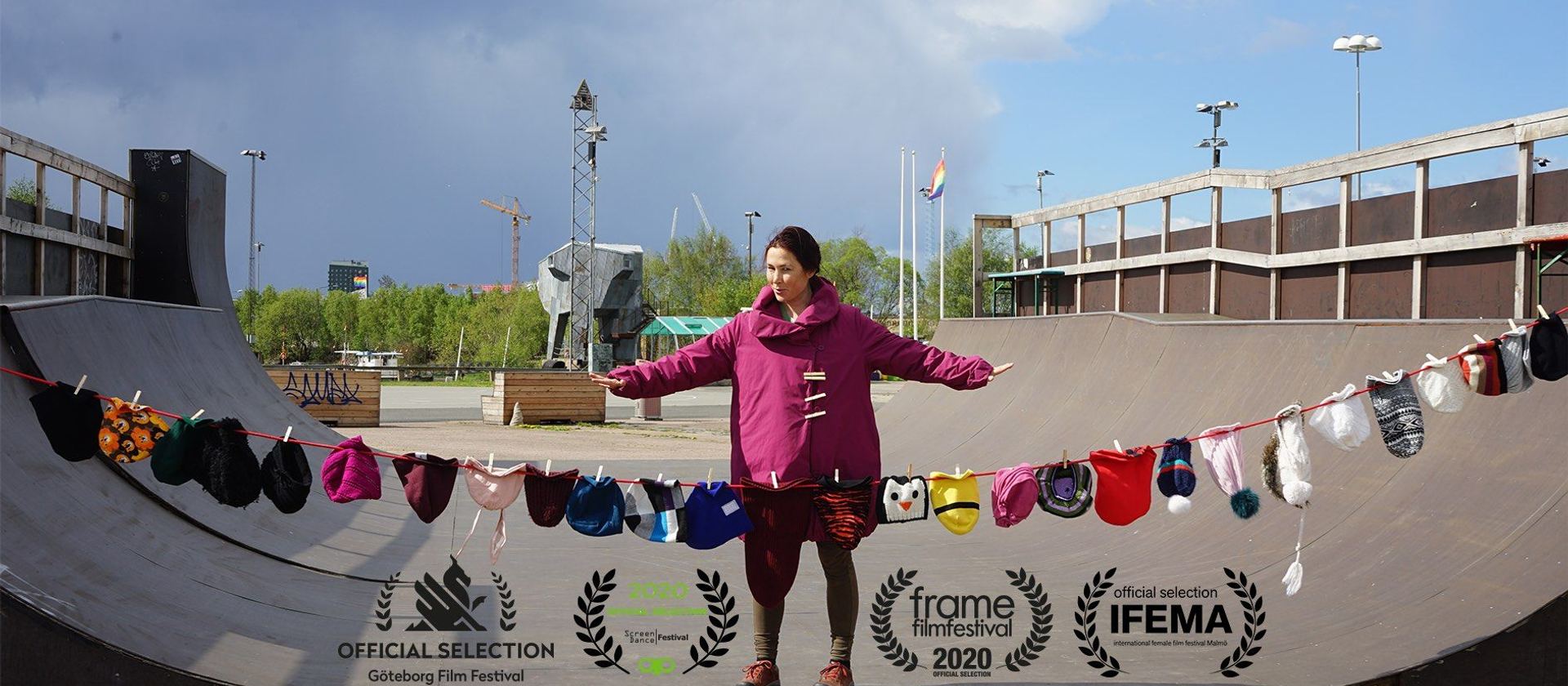 Stine står med utsträckta armar på en skateramp, med tvättlinor av små barnplagg uppspända framför sig.