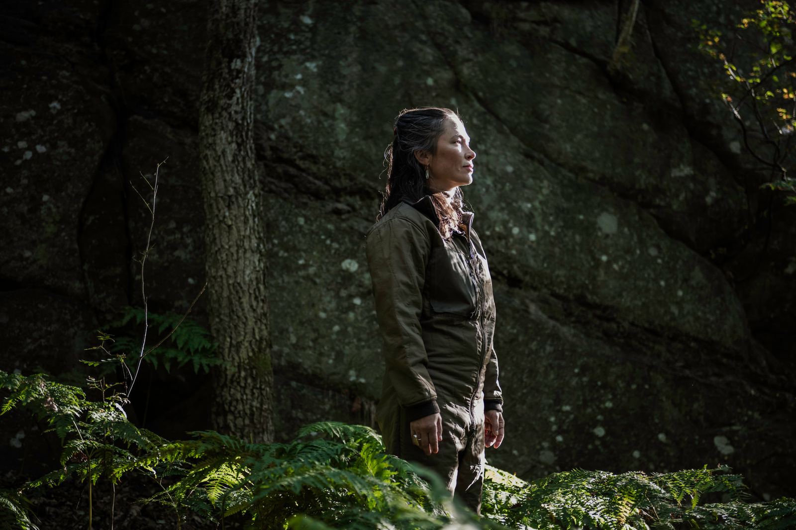 Stine står vid en mossbeklädd klippa i skogen och blickar uppåt.