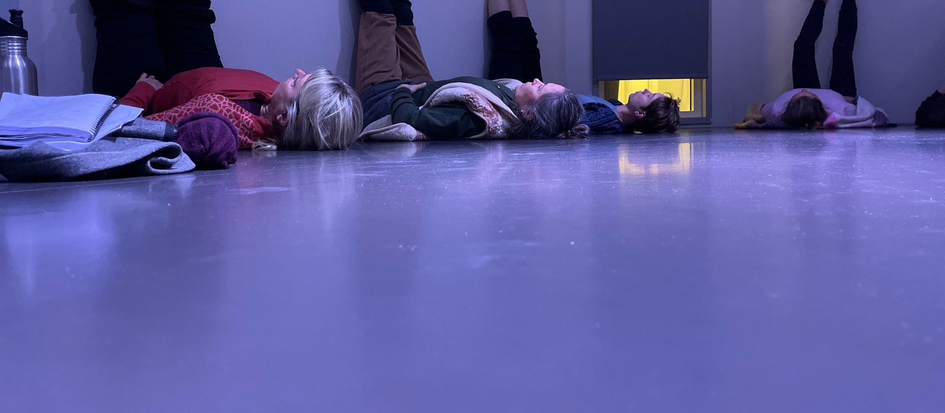 Deltagare ligger på rygg på ett studiogolv i violett ljus, med benen upp mot väggen.