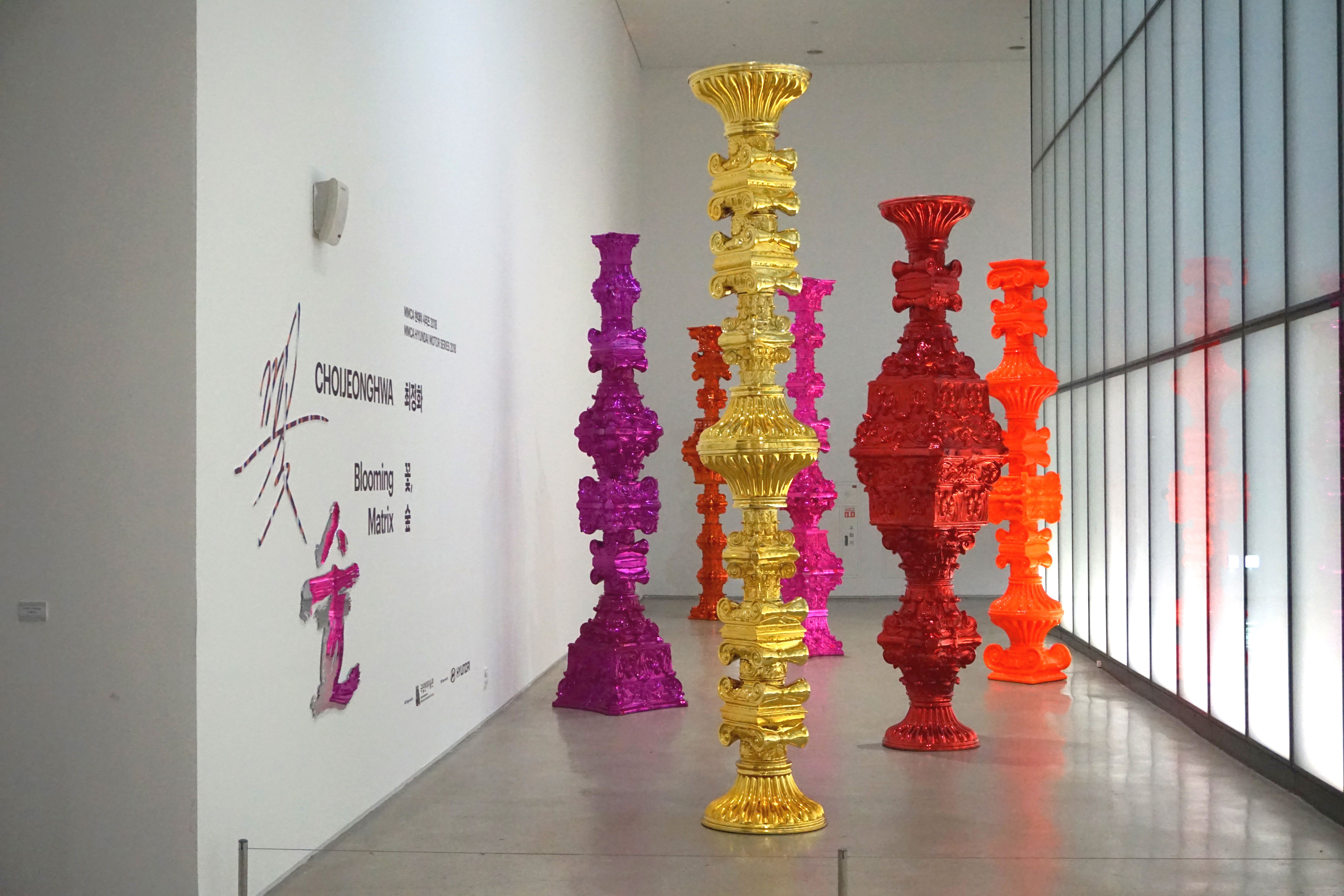 Gold, red, and purple structures with intricate designs are displayed in a spacious art gallery.