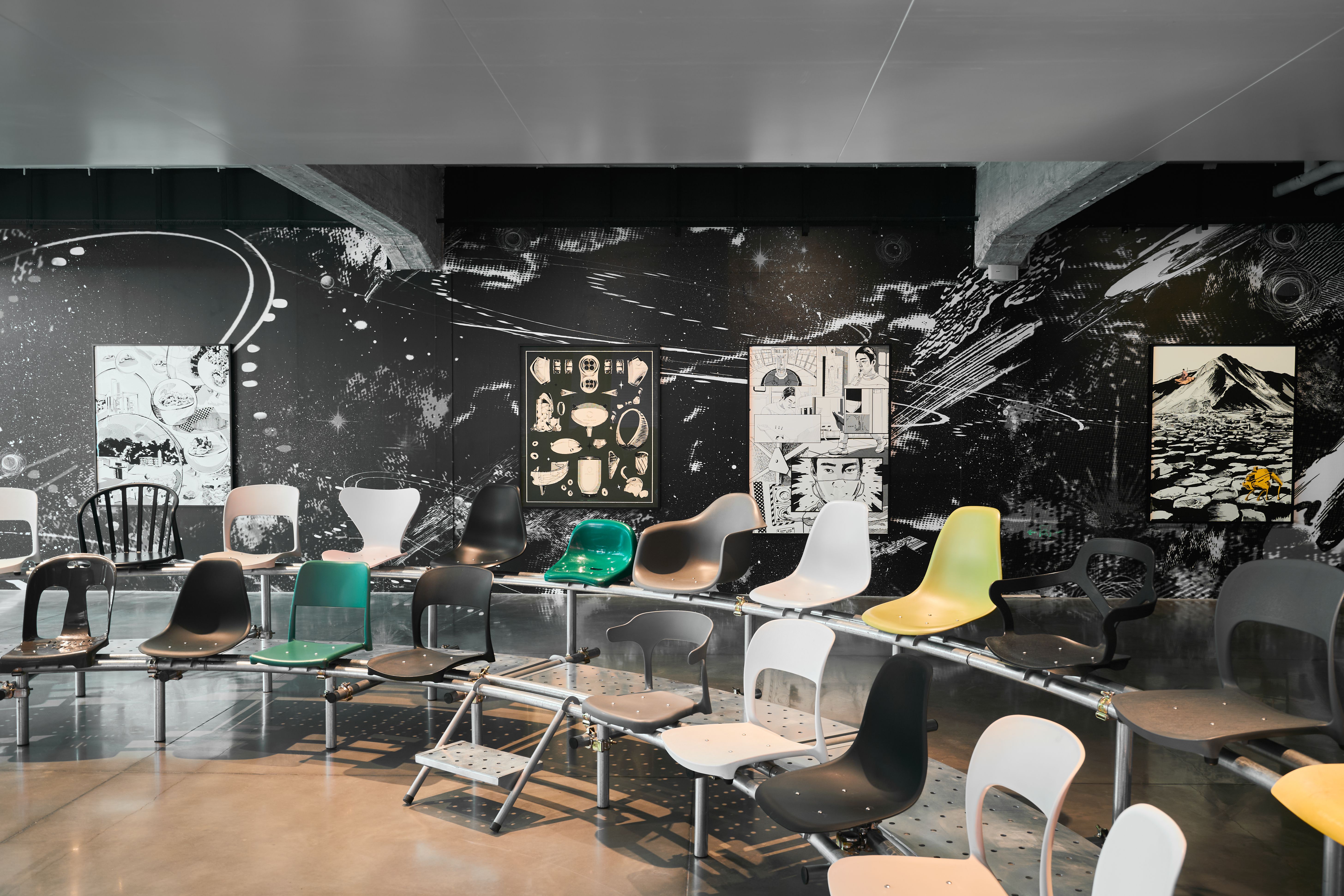 A contemporary exhibition space with a large mural featuring abstract cosmic themes. The room has a variety of colorful, m...