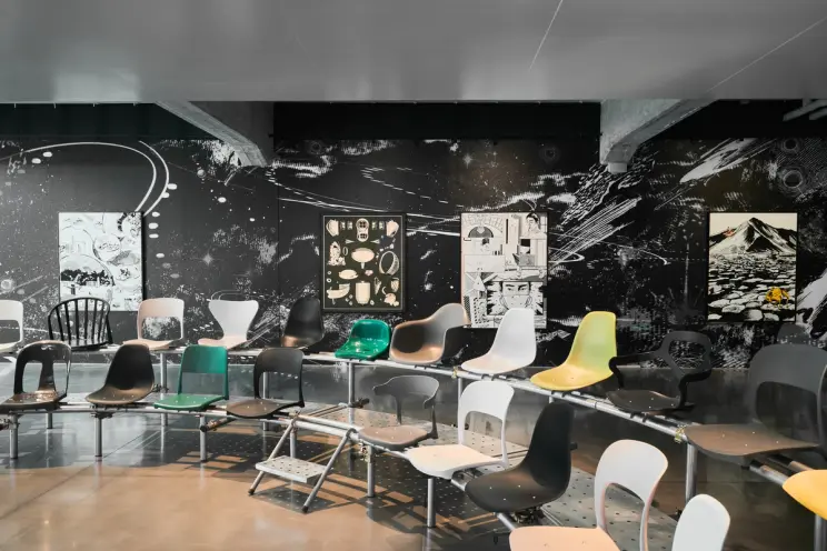 A contemporary exhibition space with a large mural featuring abstract cosmic themes. The room has a variety of colorful, m...