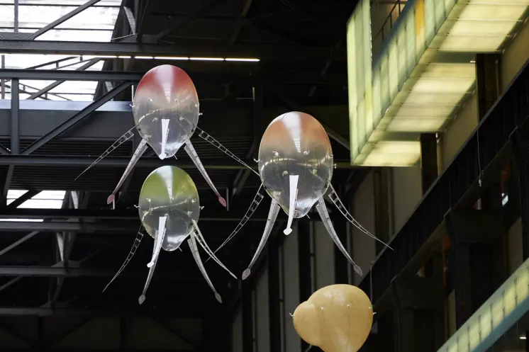 An industrial-style ceiling installation resembling an octopus with snake-headed tentacles, displayed against a dimmed bac...
