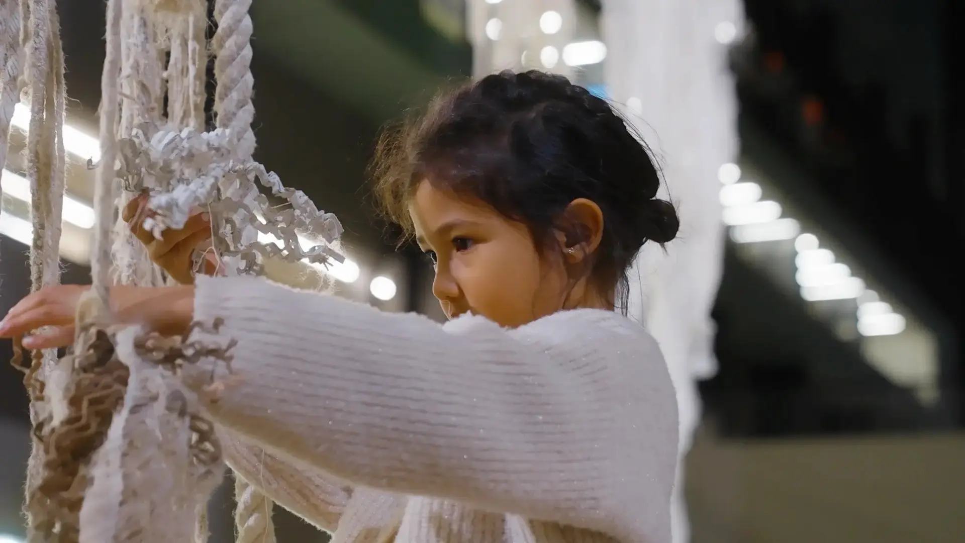 A young individual is engaged with manipulating ropes and various materials that are suspended from above.