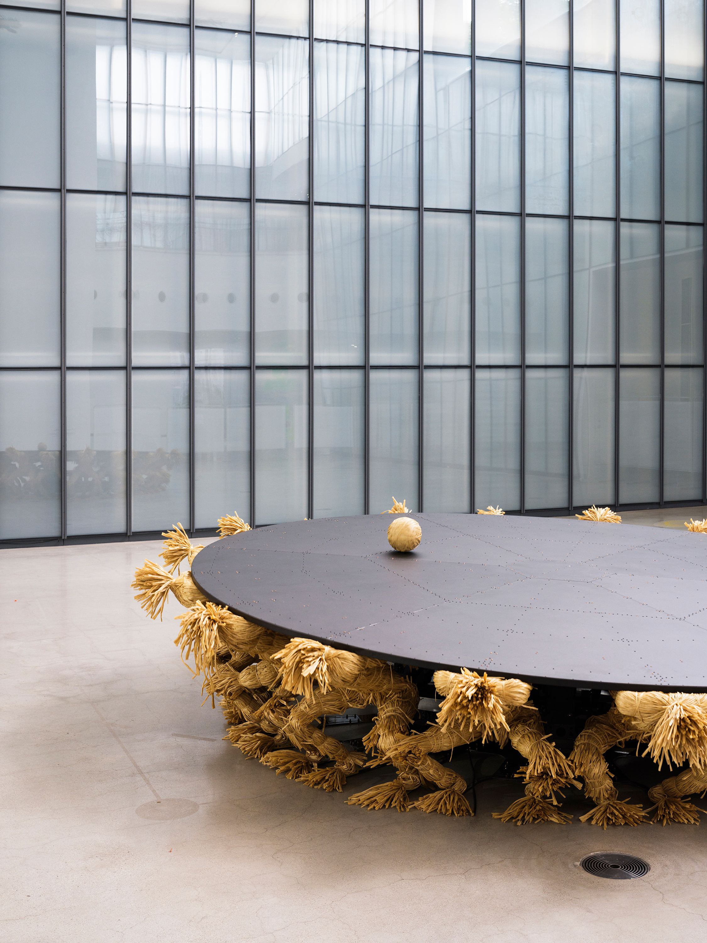An aluminim round table supported by composite material shaped like humans, with a ball on surface.