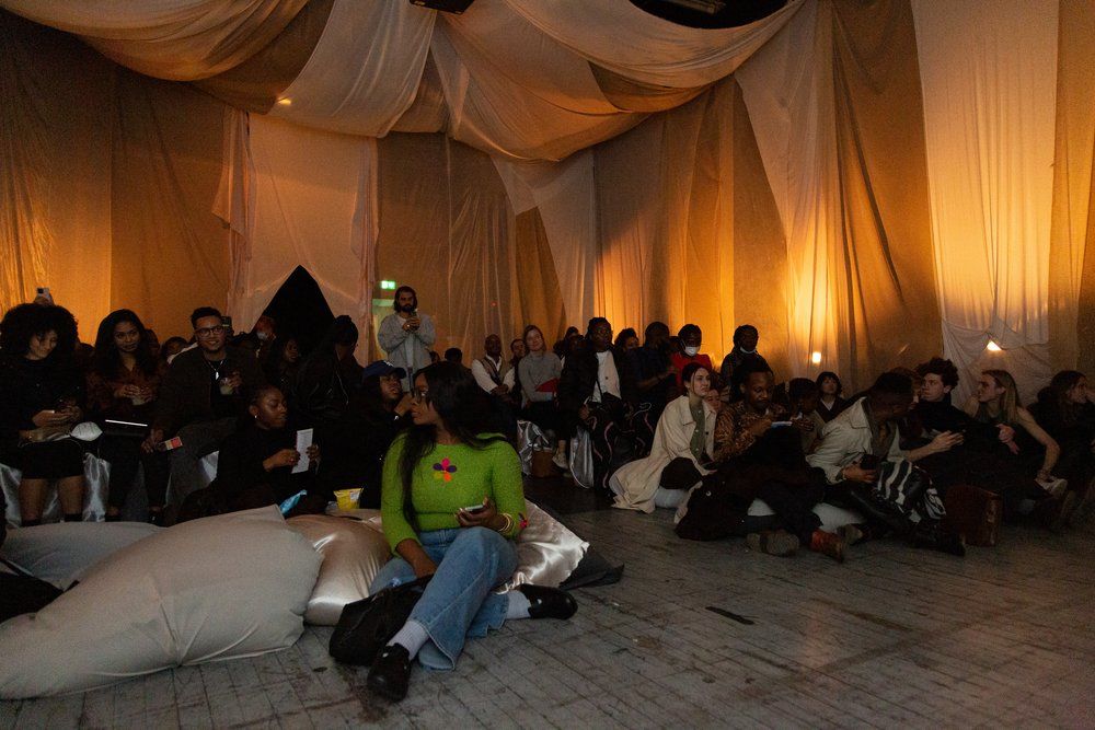 An audience seated on cushions, engaged in a presentation in a room draped with soft, glowing curtains.