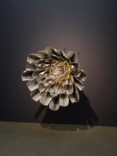 A wall-mounted art installation, reminiscent of a blooming flower, with a bright light at the center against a black wall.