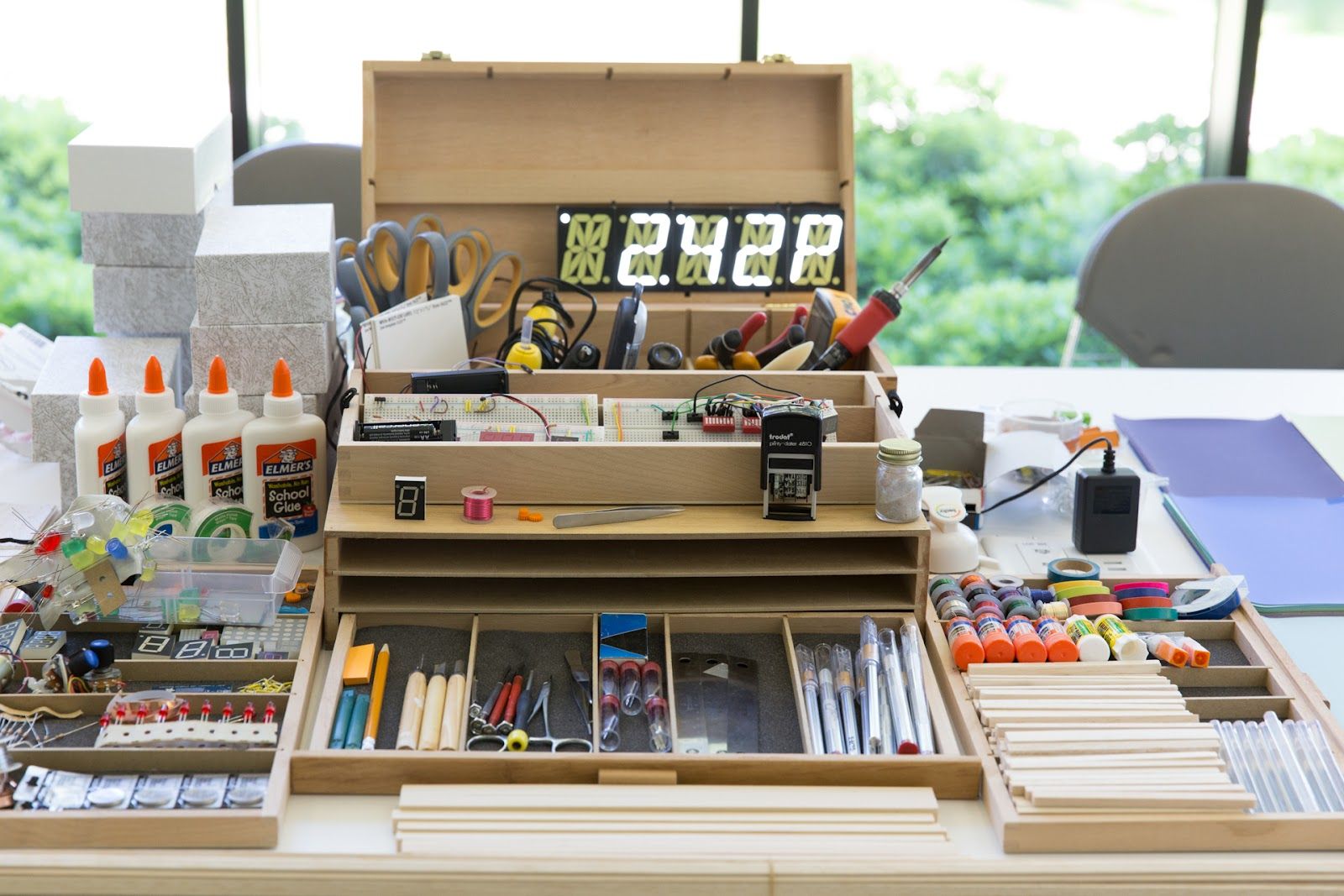 A digital arts and crafts project spread across a table, featuring a breadboard, glue, and various small parts organized i...