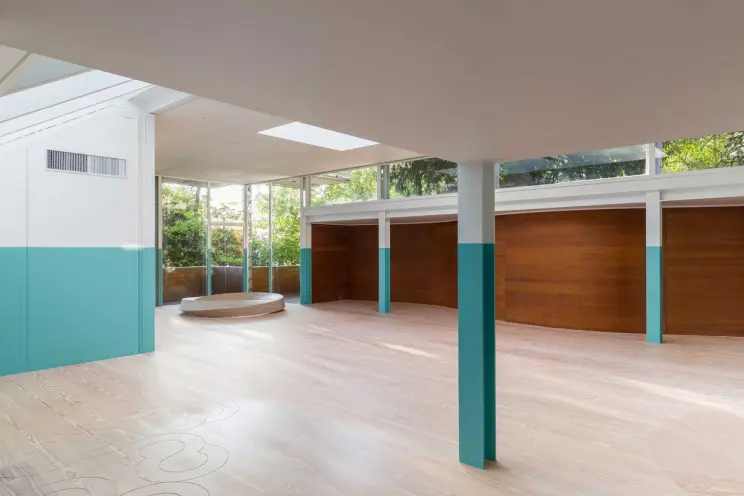 Interior view of a modern room with white and teal walls, light wooden flooring, and a wooden ring sculpture in the corner.