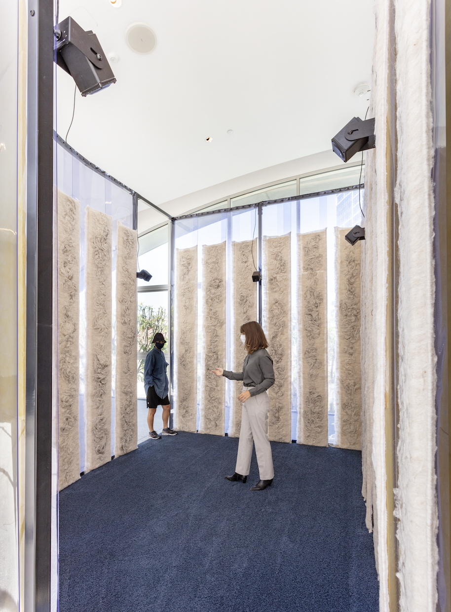 A person stands amidst an art installation with blue flooring and drapery walls, creating a distinct sense of depth and te...