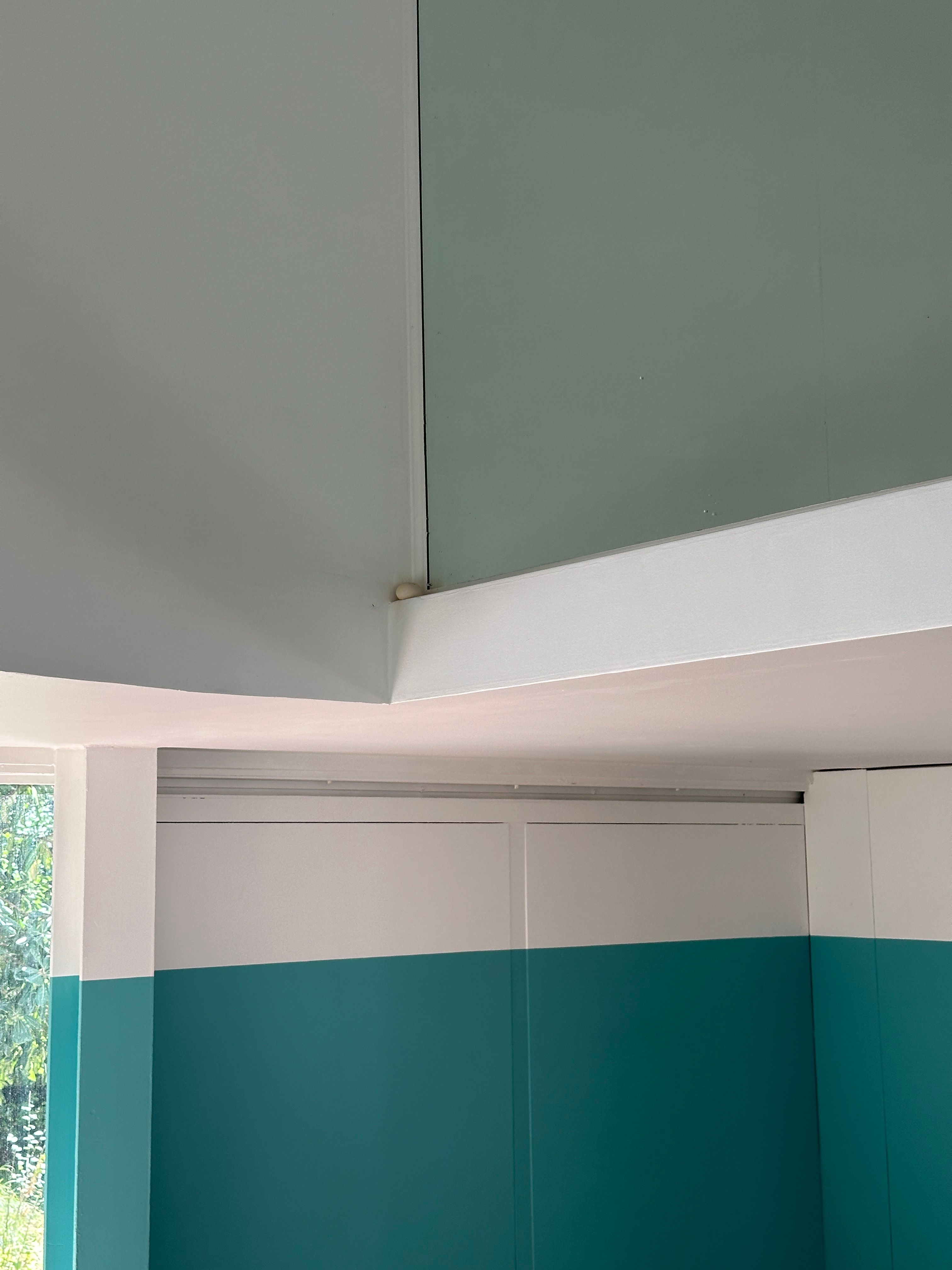 Corner view of teal and white walls in a minimalist space with soft natural lighting.