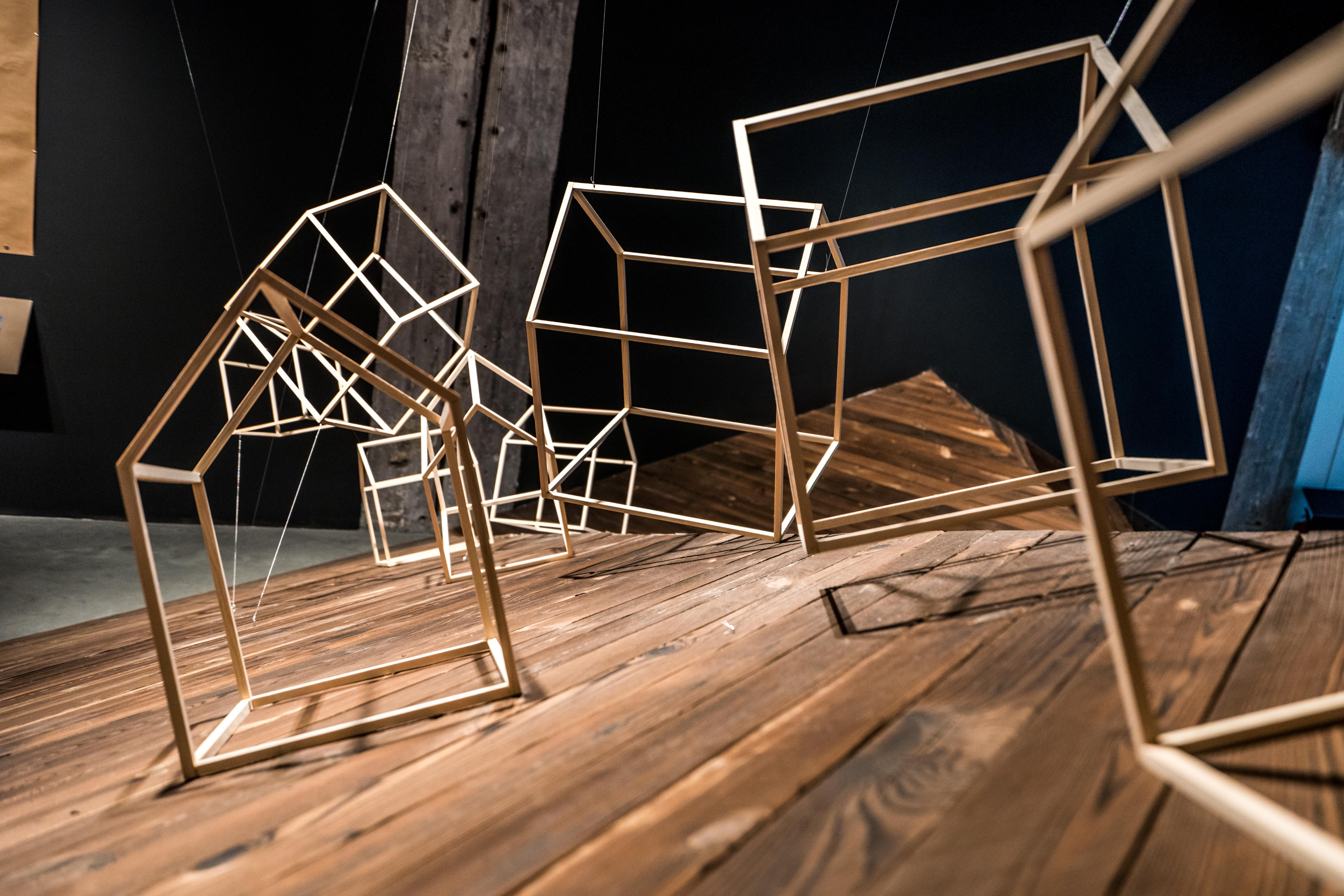 Sculptural installation of wireframe house shapes on wood.