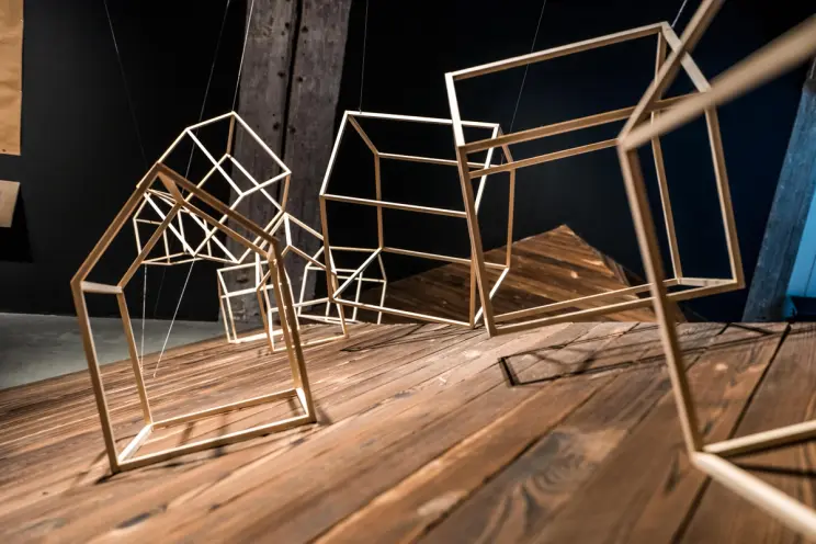 Sculptural installation of wireframe house shapes on wood.