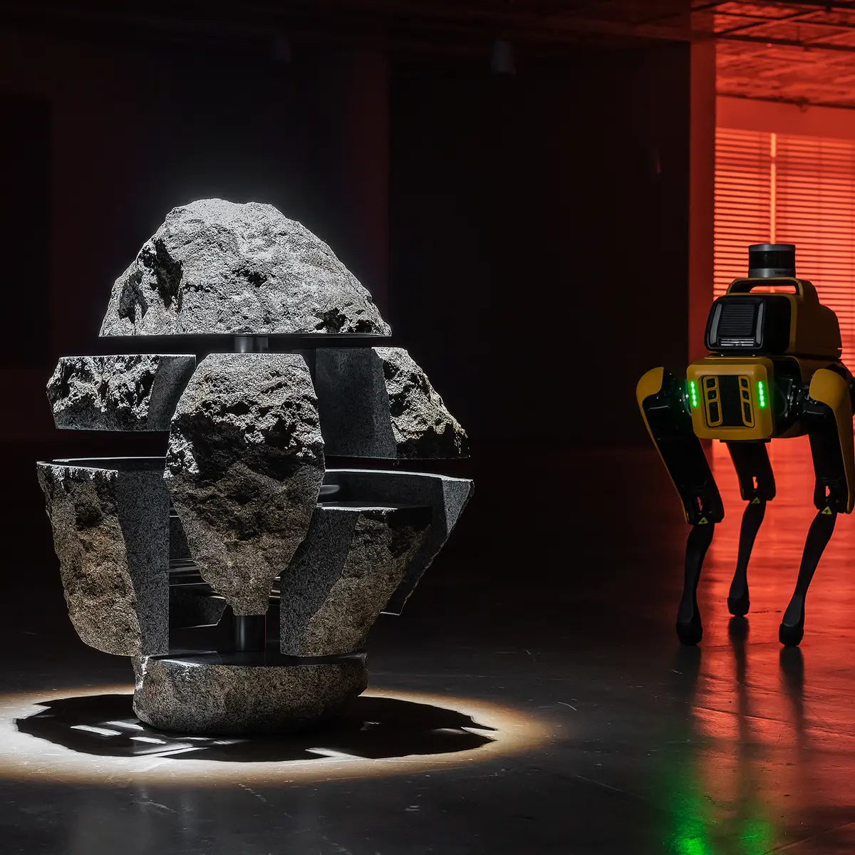 A four-legged robot examines a rock puzzle installation, bathed in the glow of an atmospheric red light in the background.