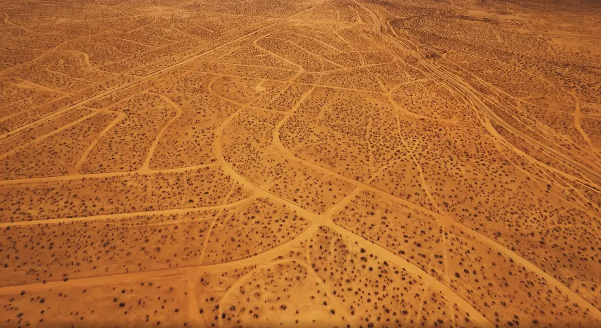 A brown desert landscape displaying a grid-like layout of paths marked by car traces.