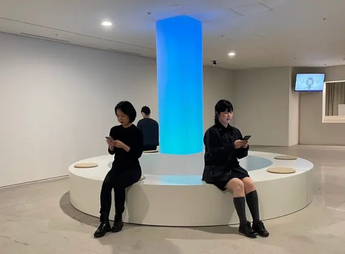 People sit on a white circular bench while using their smart phones.
