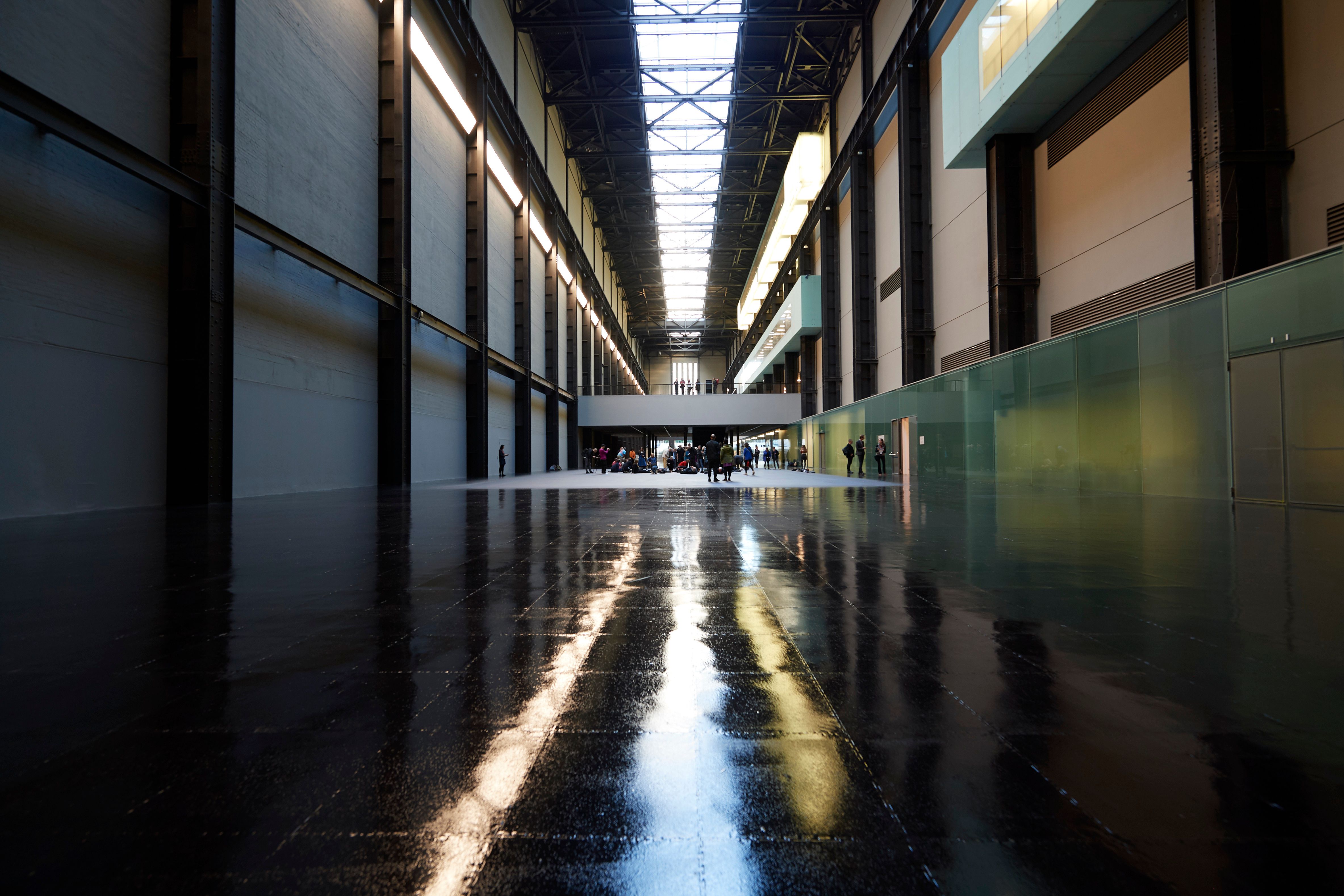 A long gallery hall with shiny dark floors is filled with visitors. The photo showcases an interior balcony floor with peo...