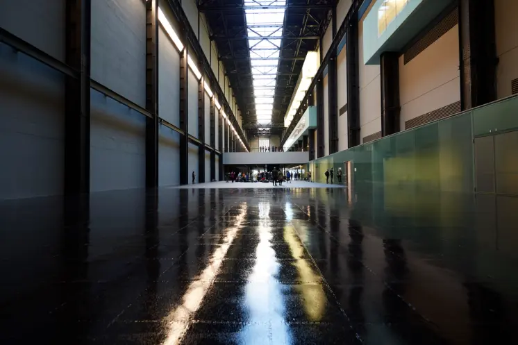A long gallery hall with shiny dark floors is filled with visitors. The photo showcases an interior balcony floor with peo...