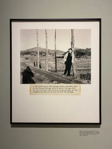 A framed digital print of a vintage photograph featuring an individual leaning on a tree in an open field. Typed caption i...