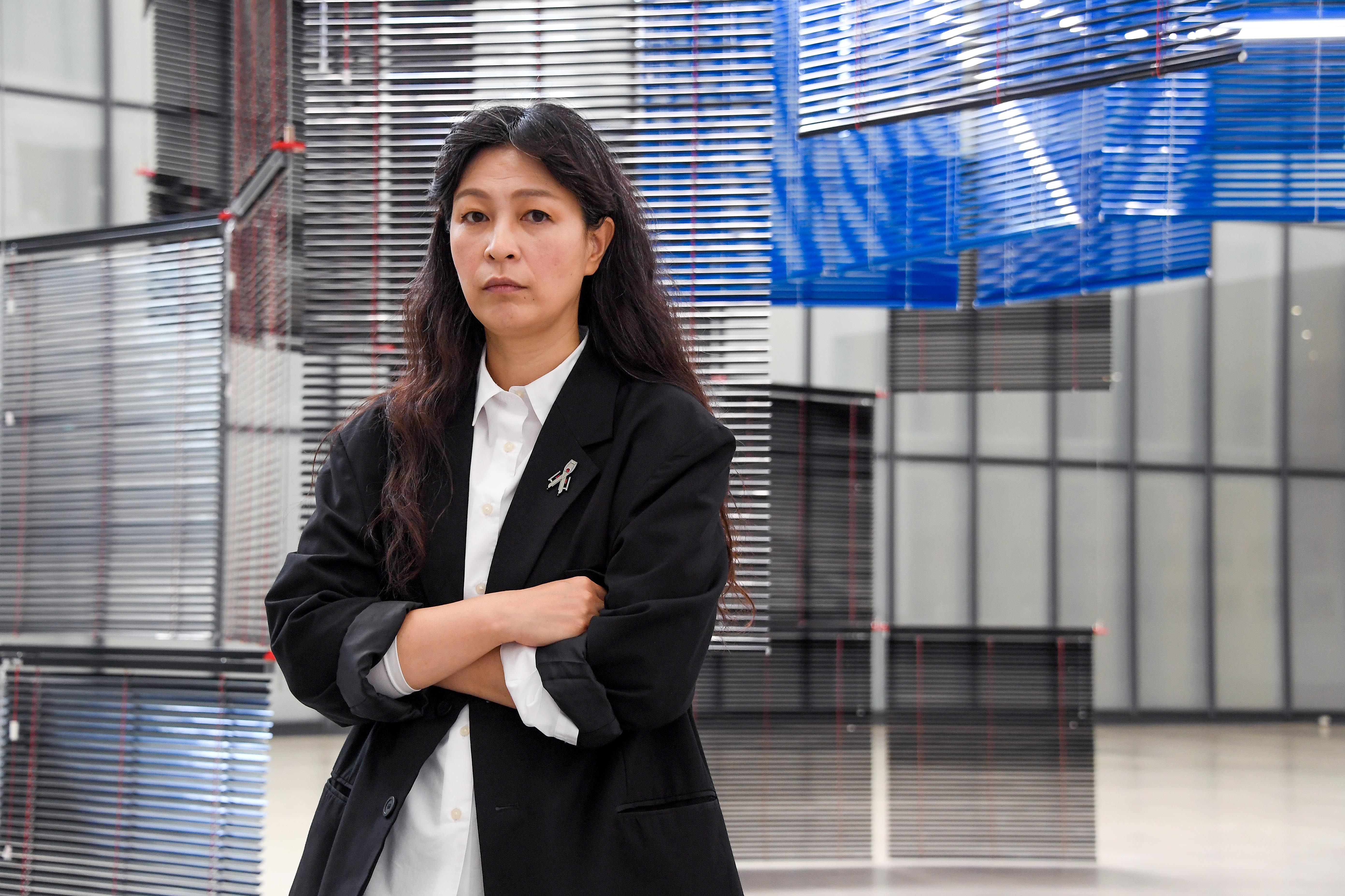 Artist Haegue Yang poses thoughtfully in front of their intricate art installation.