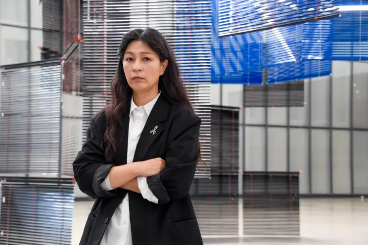 Artist Haegue Yang poses thoughtfully in front of their intricate art installation.