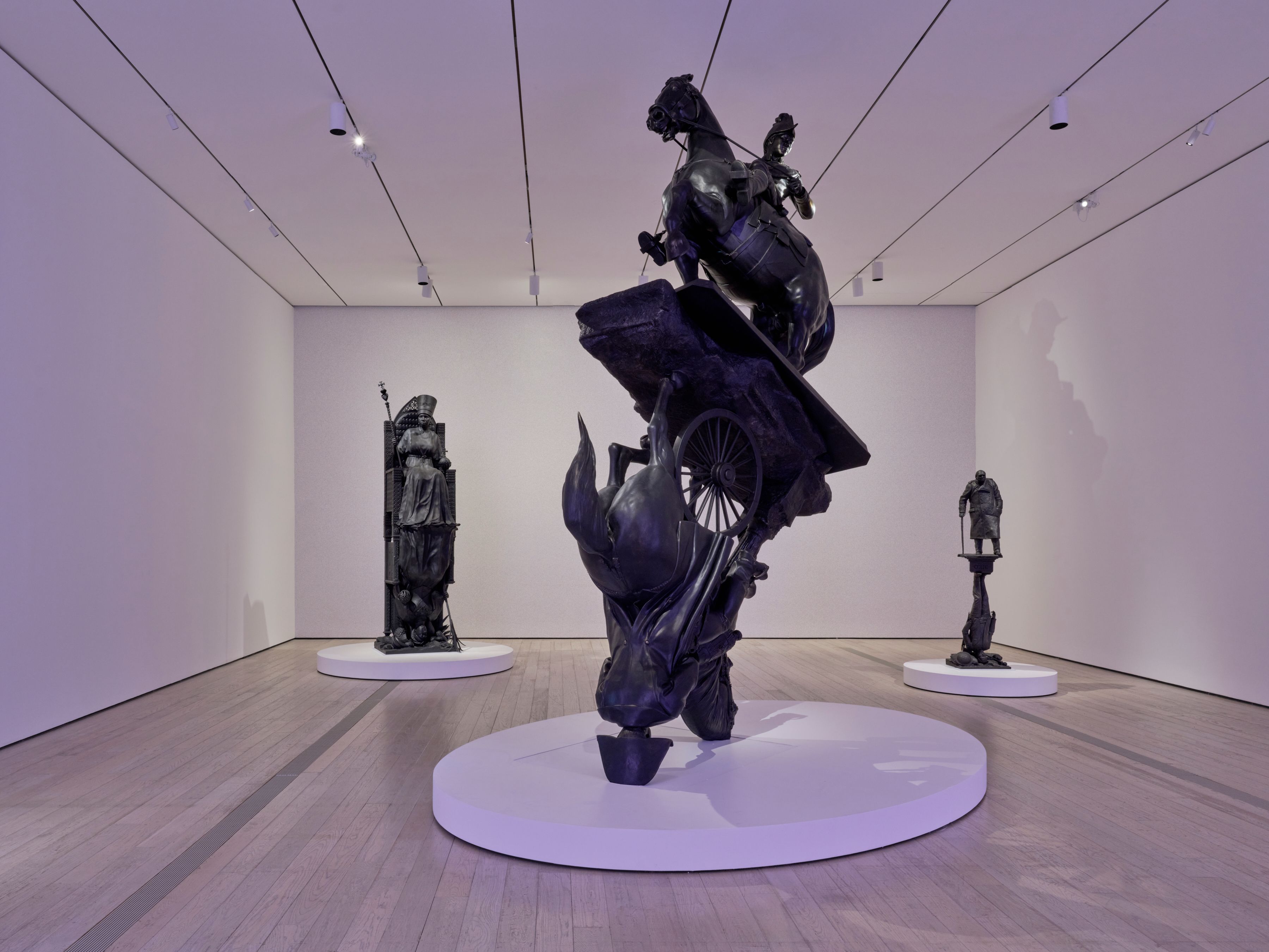 Gallery with dramatic dark bronze sculptures on white platforms, including a rearing horse and towering figures.