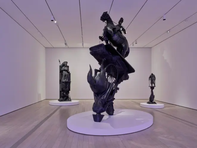 Gallery with dramatic dark bronze sculptures on white platforms, including a rearing horse and towering figures.
