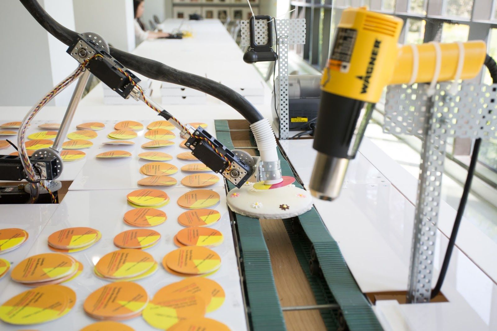 Industrial machinery operates in a factory setting, handling stacks of yellow circle pie charts with various printed texts.