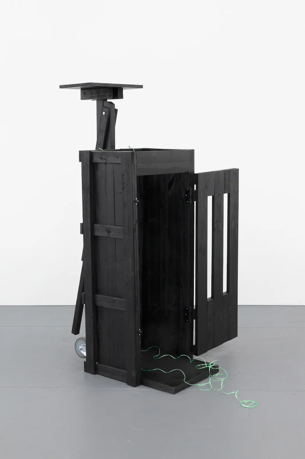 A black server rack with green wires is presented in a minimalist gallery setting.