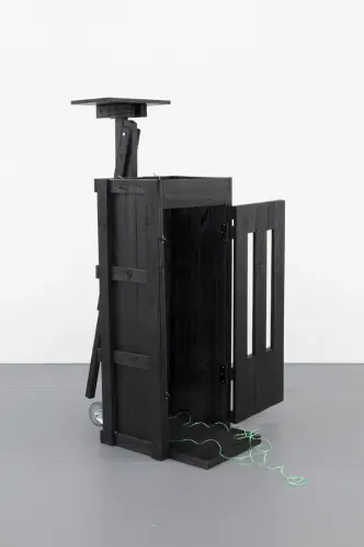 A black server rack with green wires is presented in a minimalist gallery setting.