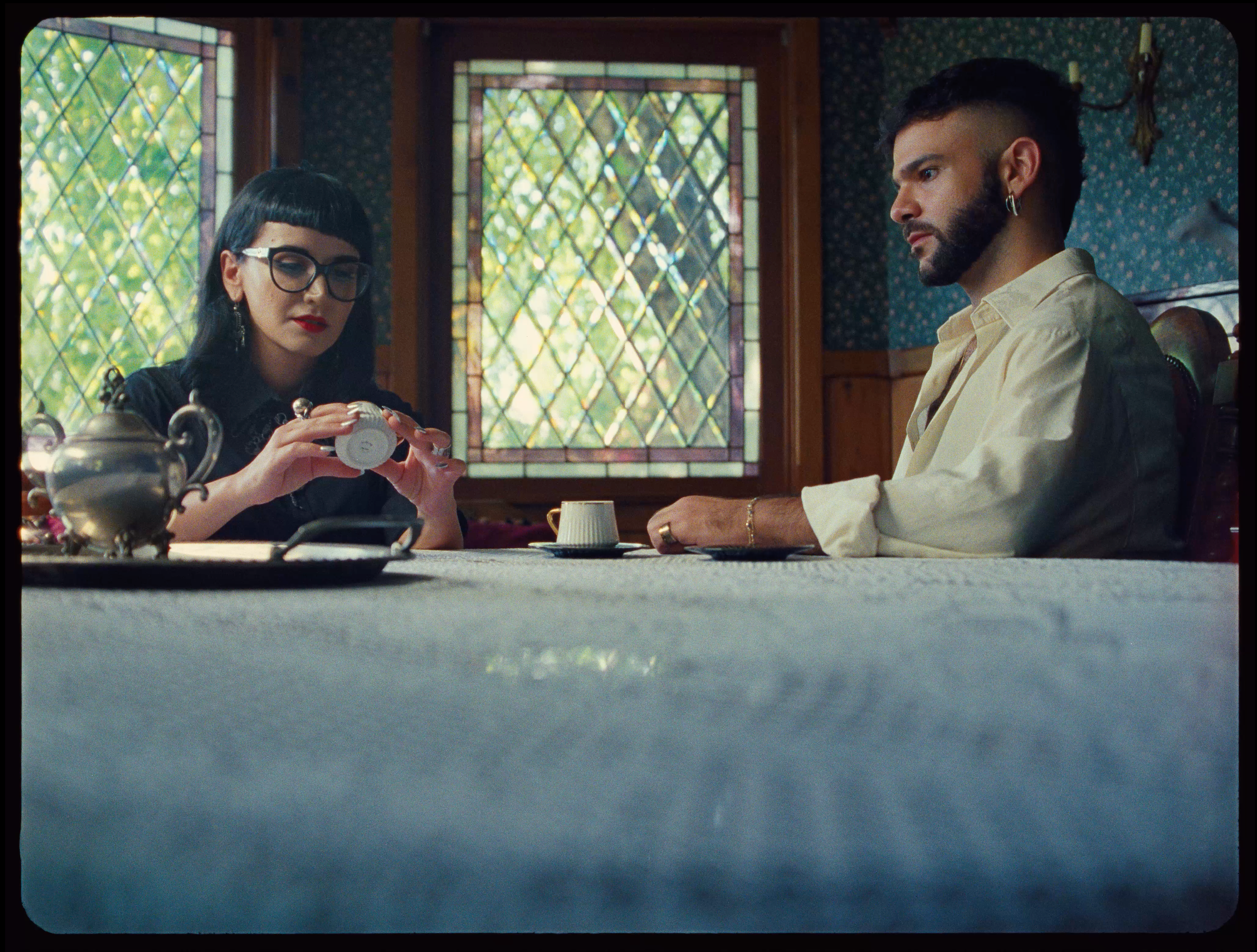 A woman and a man seated at a table, the woman examining a coffee cup while the man watches intently.