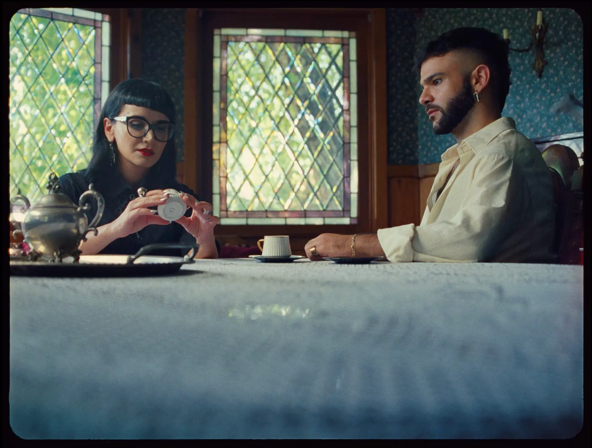 A woman and a man seated at a table, the woman examining a coffee cup while the man watches intently.