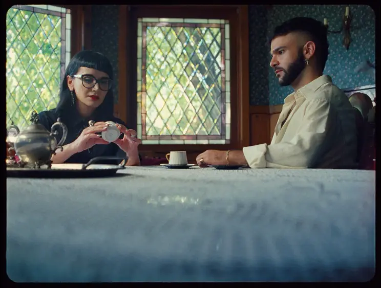 A woman and a man seated at a table, the woman examining a coffee cup while the man watches intently.