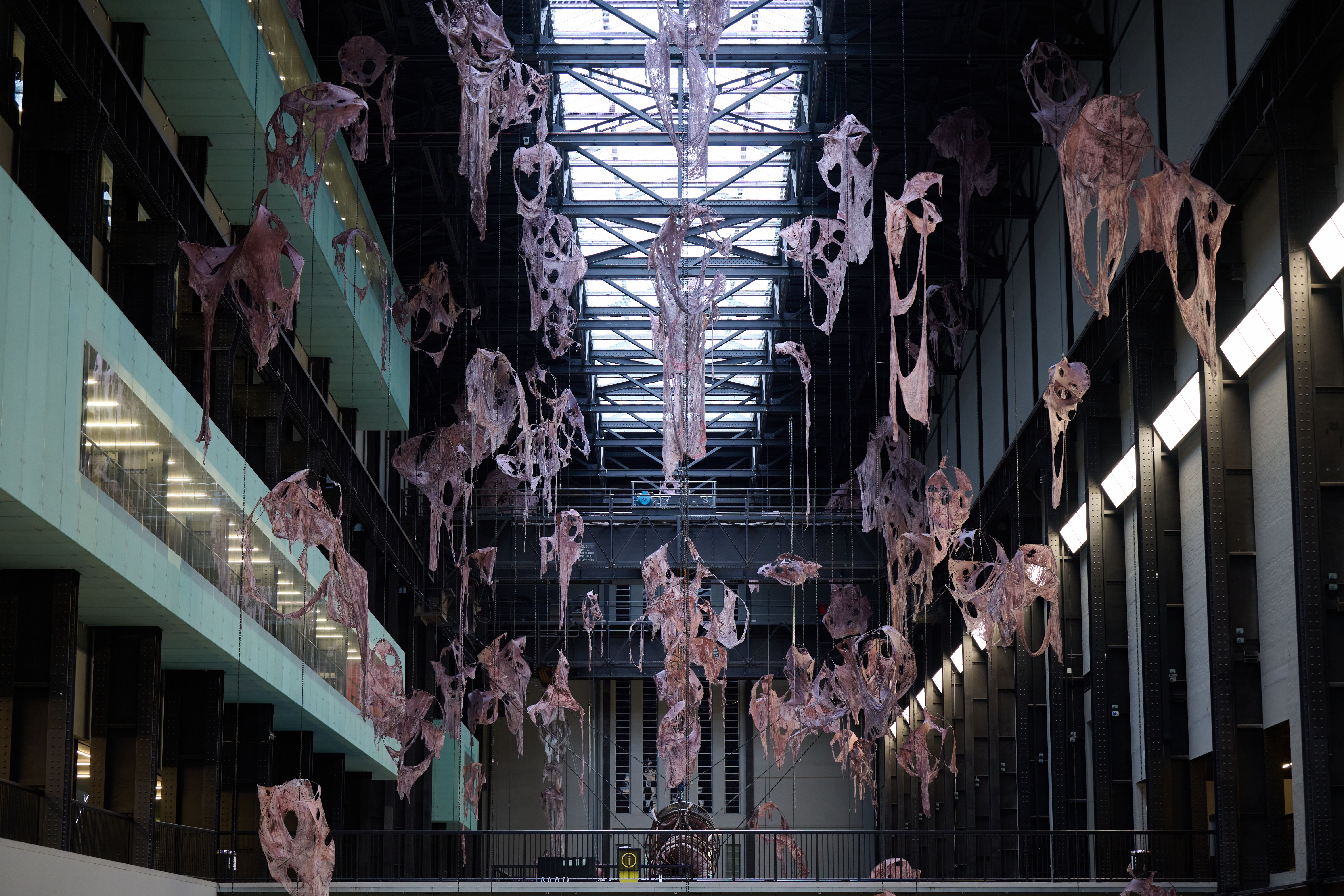 High view of installation with multiple hanging abstract organic shapes, suspended under industrial beams.