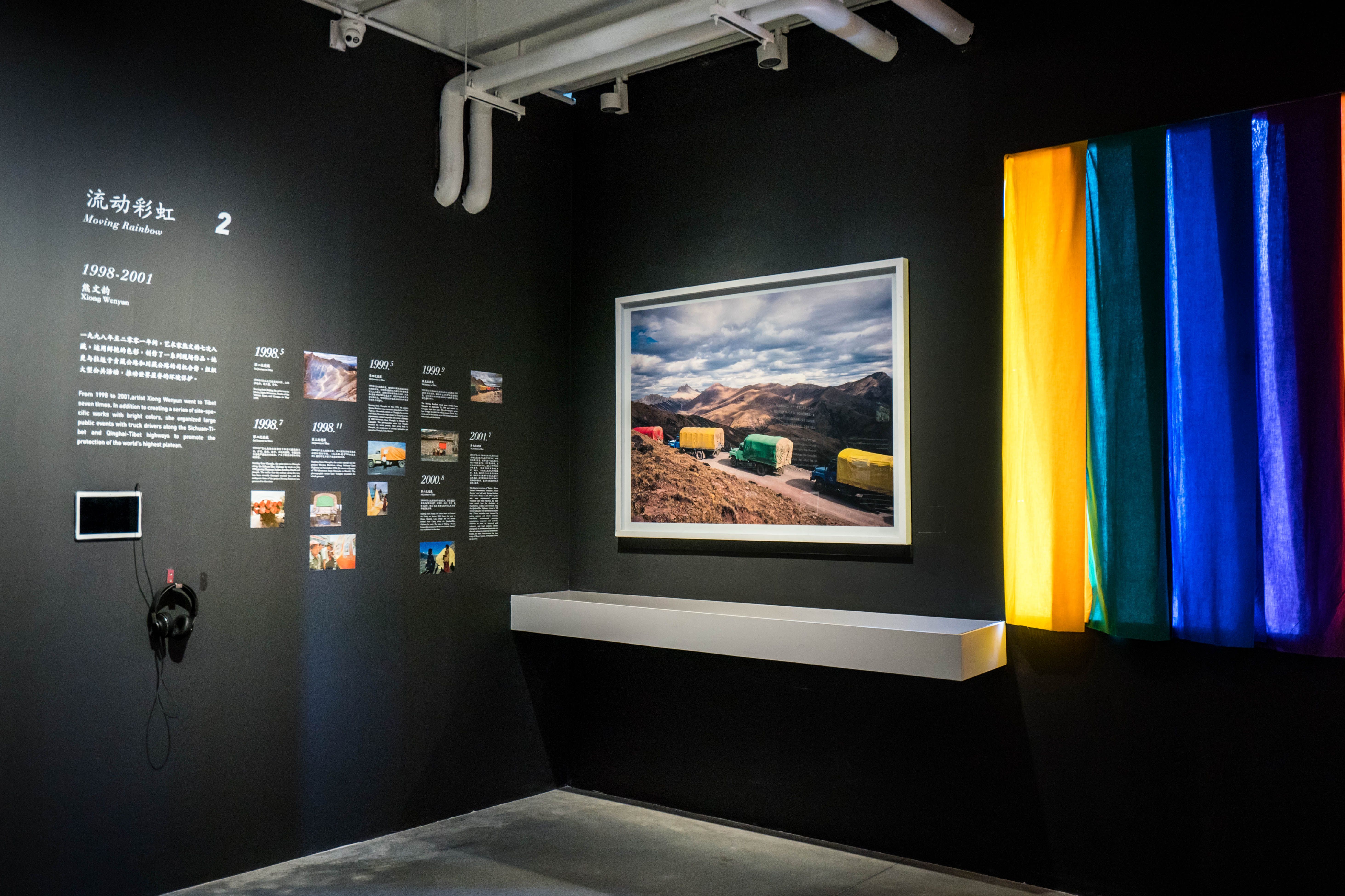 Exhibition space with colorful textile art and framed landscape photo.