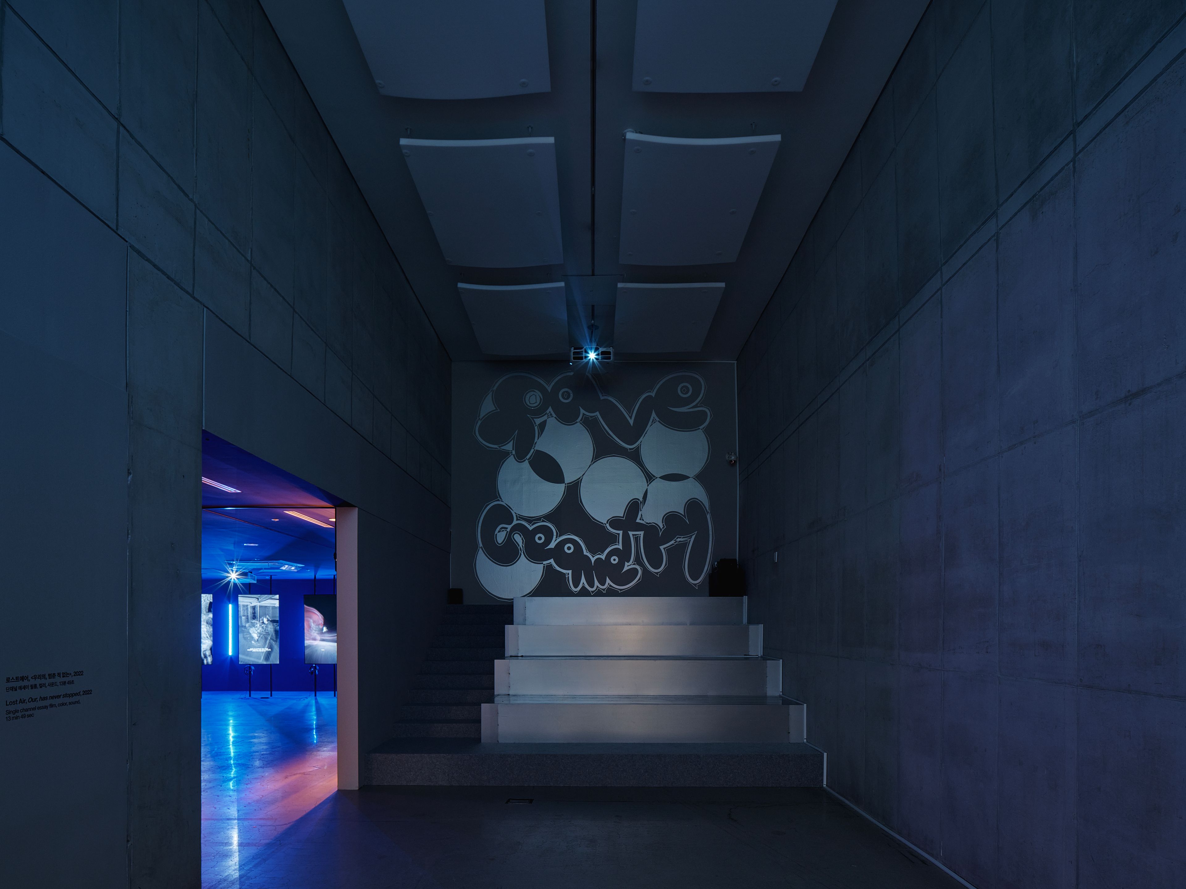 A spacious hall featuring a stairway with the text "rave geometry" displayed on the wall behind in a distinctive font. Whi...