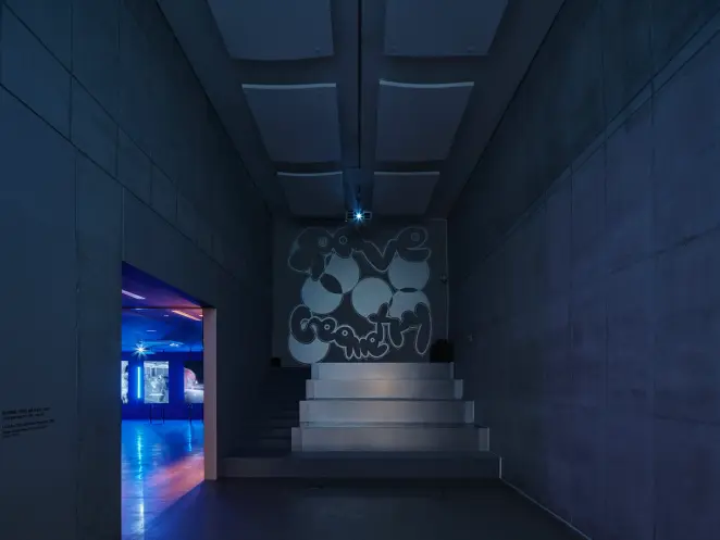 A spacious hall featuring a stairway with the text "rave geometry" displayed on the wall behind in a distinctive font. Whi...