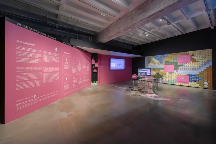 Exhibition space with pink walls featuring text and graphics, and a video display.
