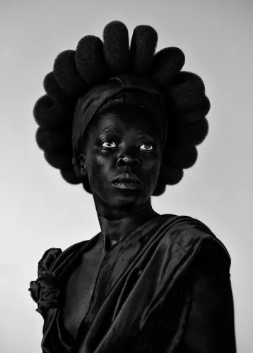 A figure in a monochrome photo, theatrically poised to mimic a black statue against a white backdrop.