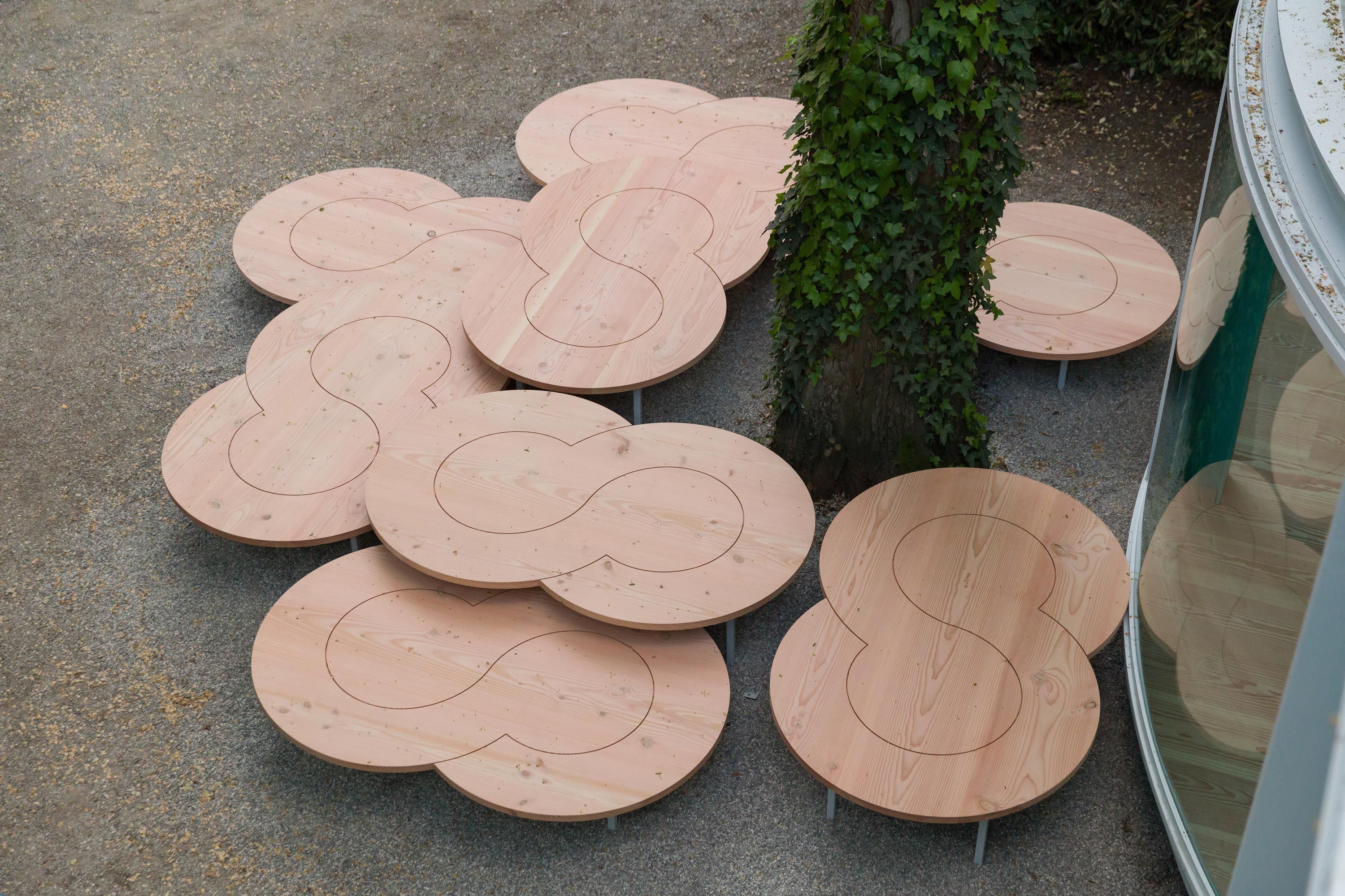 Overhead view of wooden tables near a tree by a glass pavilion, set on a gravel path.