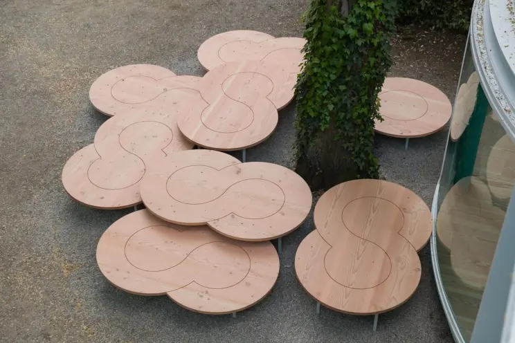 Overhead view of wooden tables near a tree by a glass pavilion, set on a gravel path.