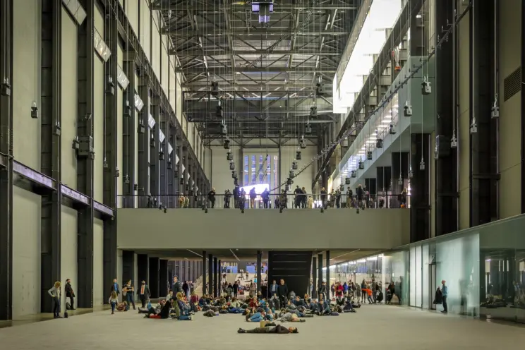 Tate Modern's Turbine Hall, a high-ceilinged gallery space, filled with individuals in various positions such as standing,...