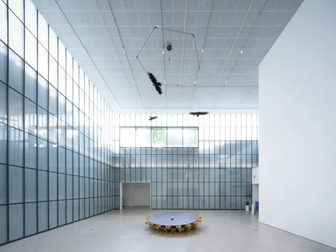 A bright room with window panels housing an art installation: a hemispheric table with a wooden ball at the center, and ea...