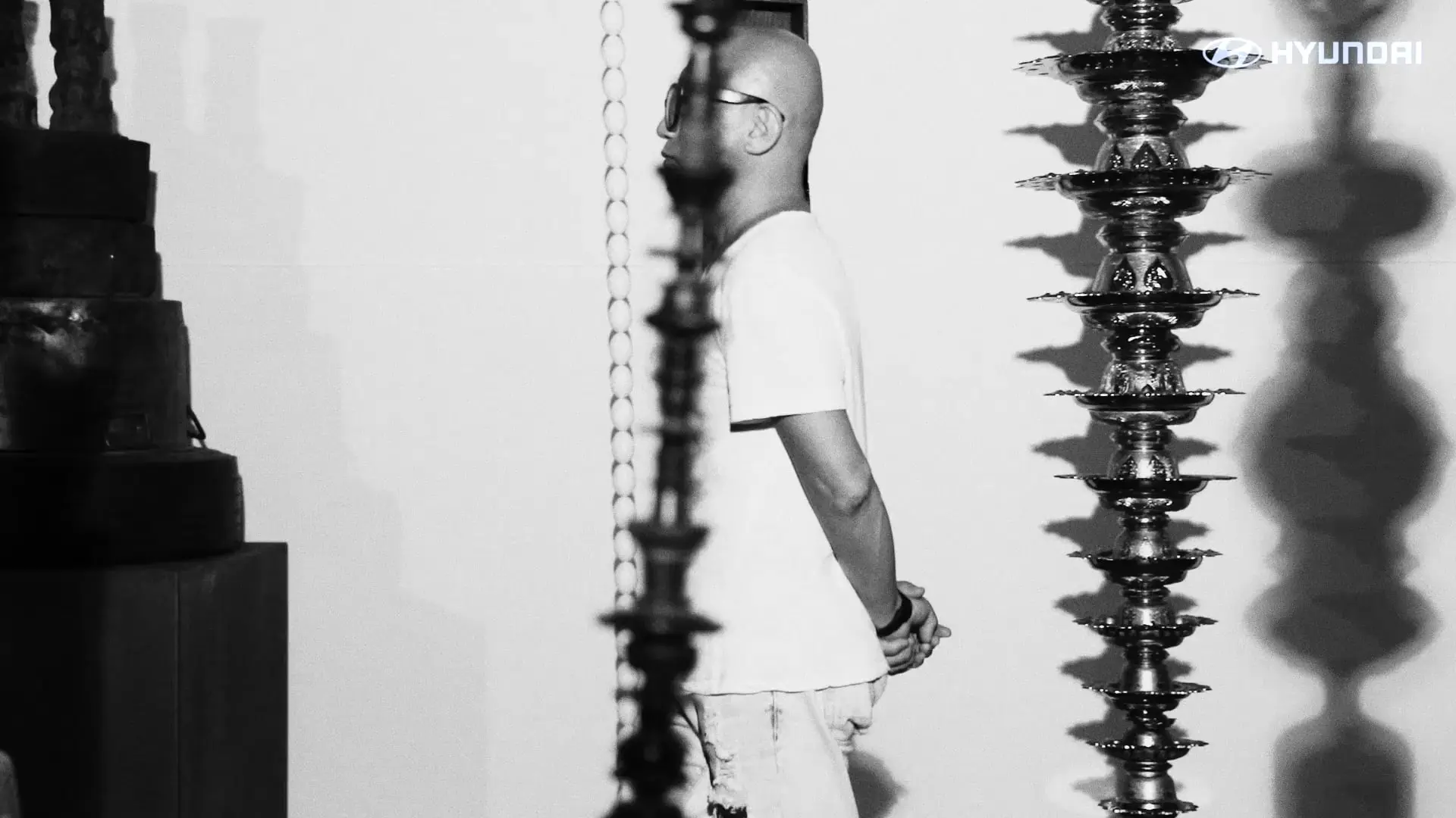 Profile of a man in a white T-shirt, standing contemplatively next to intricate metal sculptures with a shadow cast on a ...