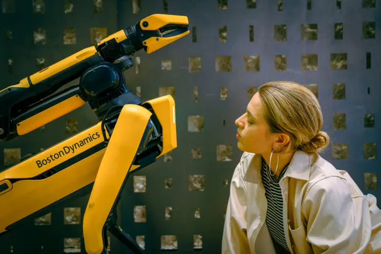A person closely examines a Boston Dynamics robot arm, showcasing a human-robot interaction.