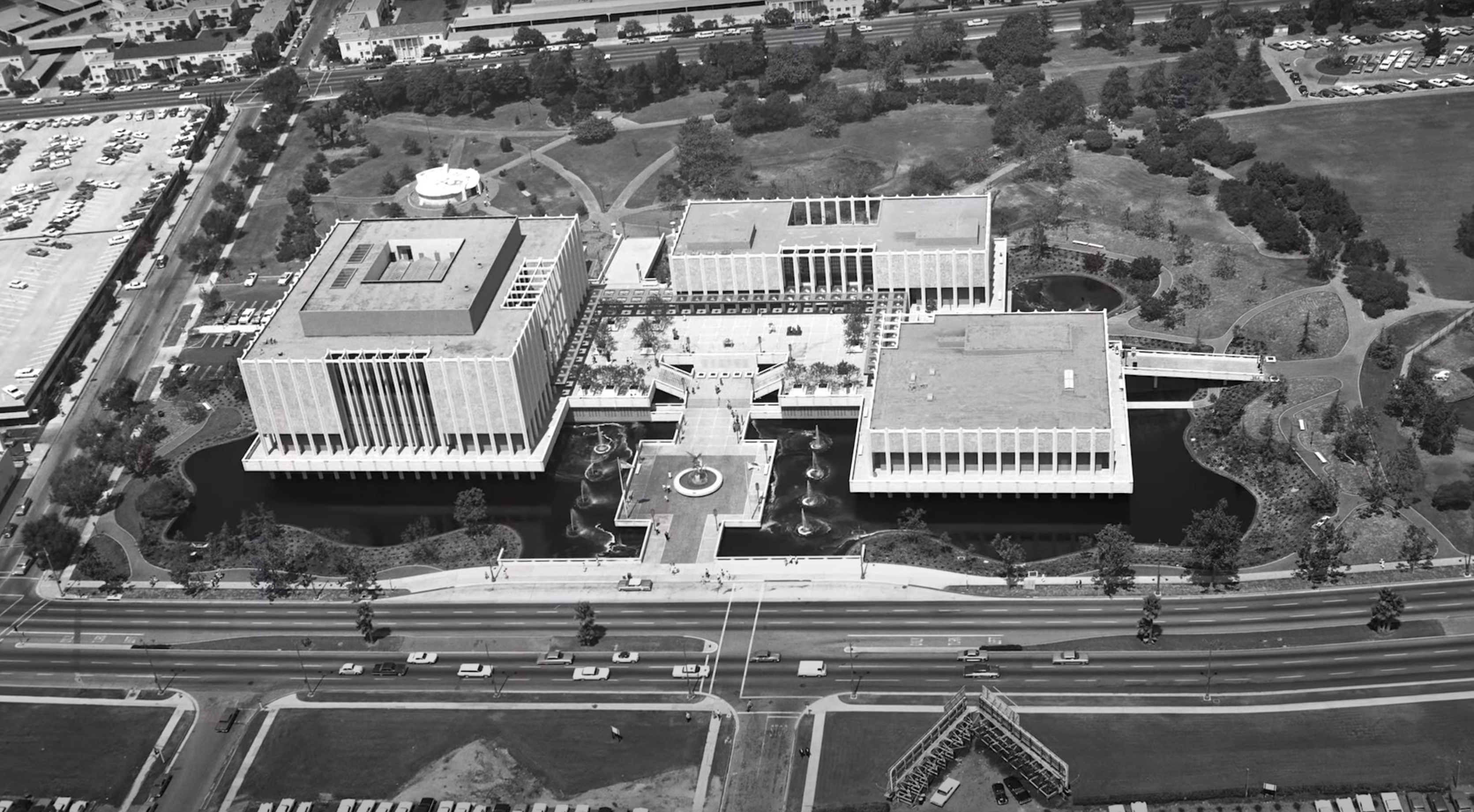 An aerial black-and-white photograph showcases an urban landscape, including buildings, roads, and cars. Infrastructure an...